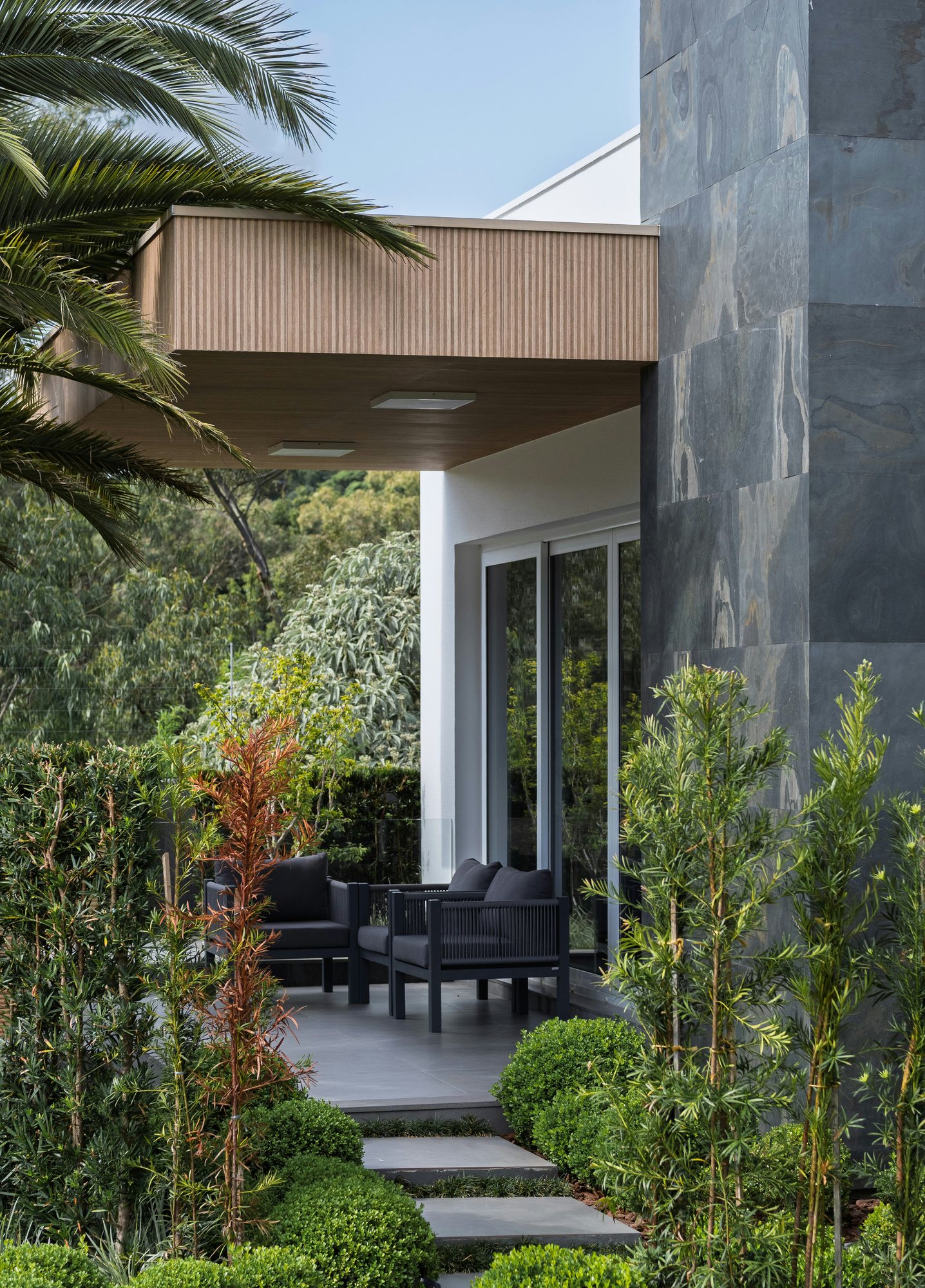 Sheltered patio at Common Ground with armchairs, a slate wall and established garden planting