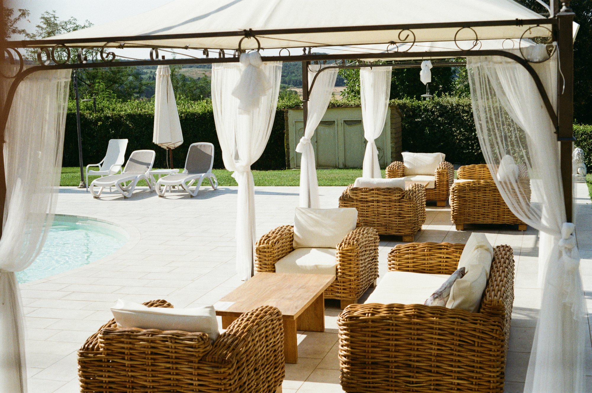 Poolside gazebo at Common Ground with white drapes and wicker lounge seating in afternoon light